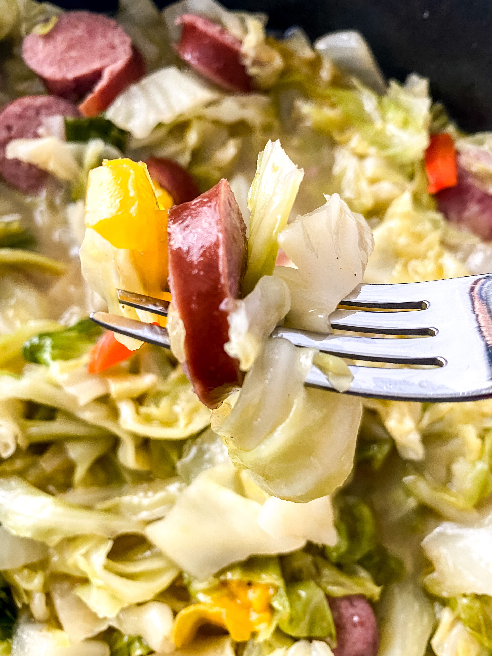 Fork holding a bite of Southern-style cabbage and smoked turkey sausage with bell peppers and onions.