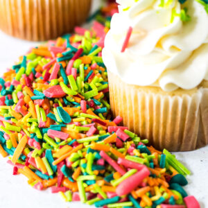 Cupcake decorated with DIY sprinkles sitting in a pile of colorful homemade sprinkles.