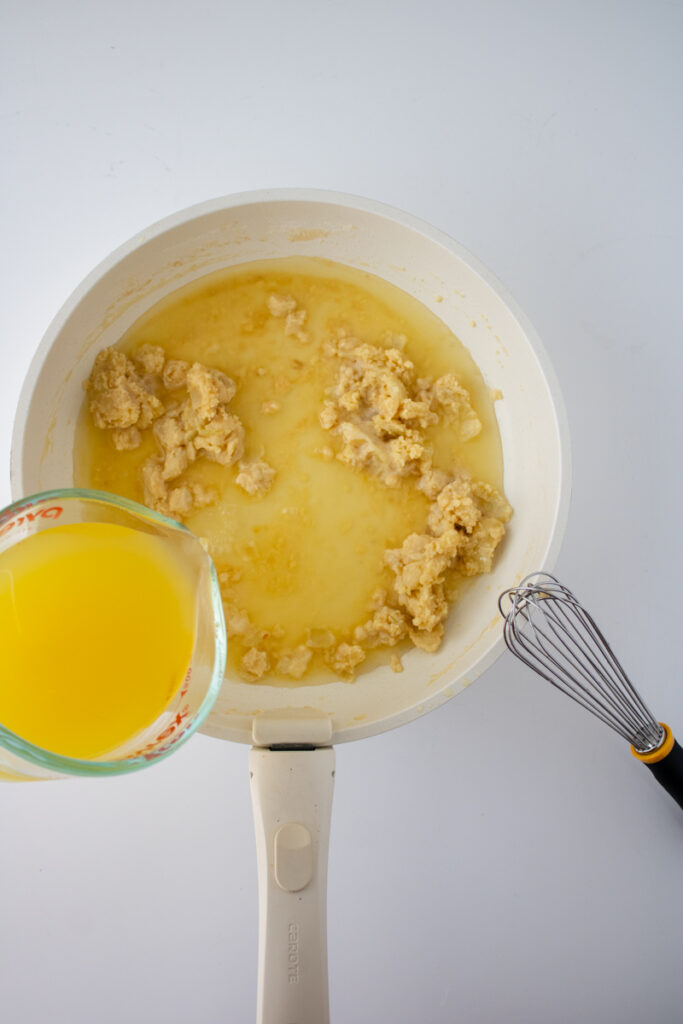 Chicken broth being added to a roux in a skillet for chicken pot pie sauce.
