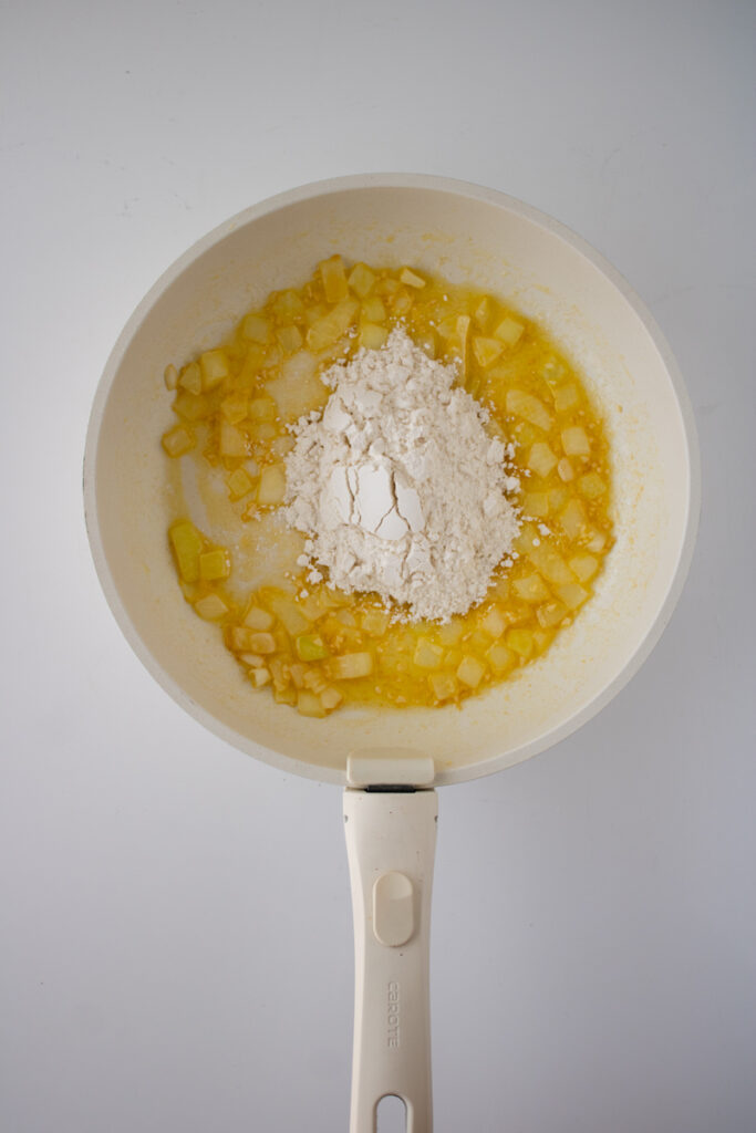 Flour added to sautéed onions and garlic in a skillet to make a roux for chicken pot pie filling.