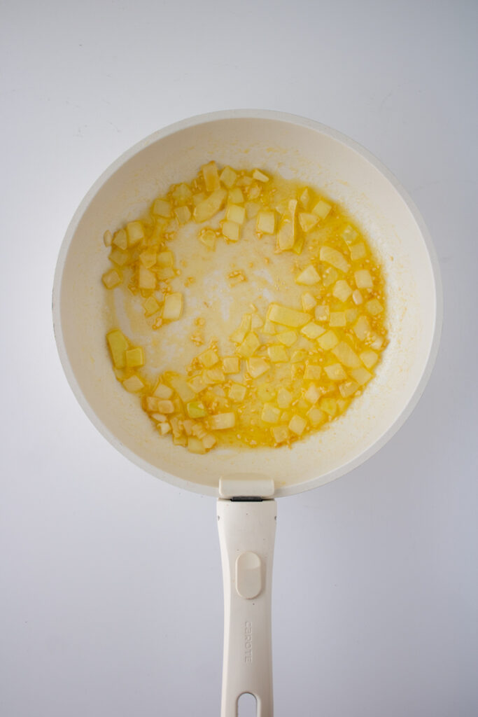 Softened onions and minced garlic cooking in butter in a skillet for chicken pot pie filling.