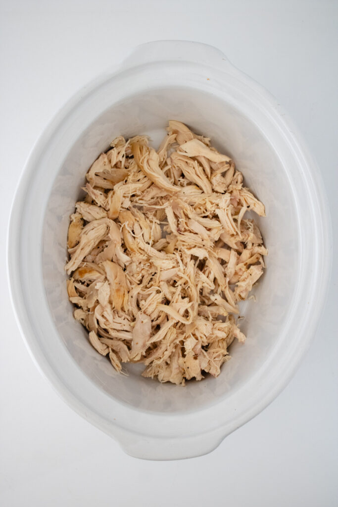 Shredded rotisserie chicken spread evenly in the bottom of a slow cooker for buffalo chicken dip.