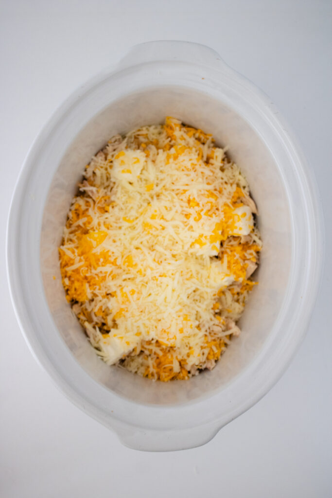Shredded cheddar and mozzarella cheese layered over chicken and cream cheese in a slow cooker.