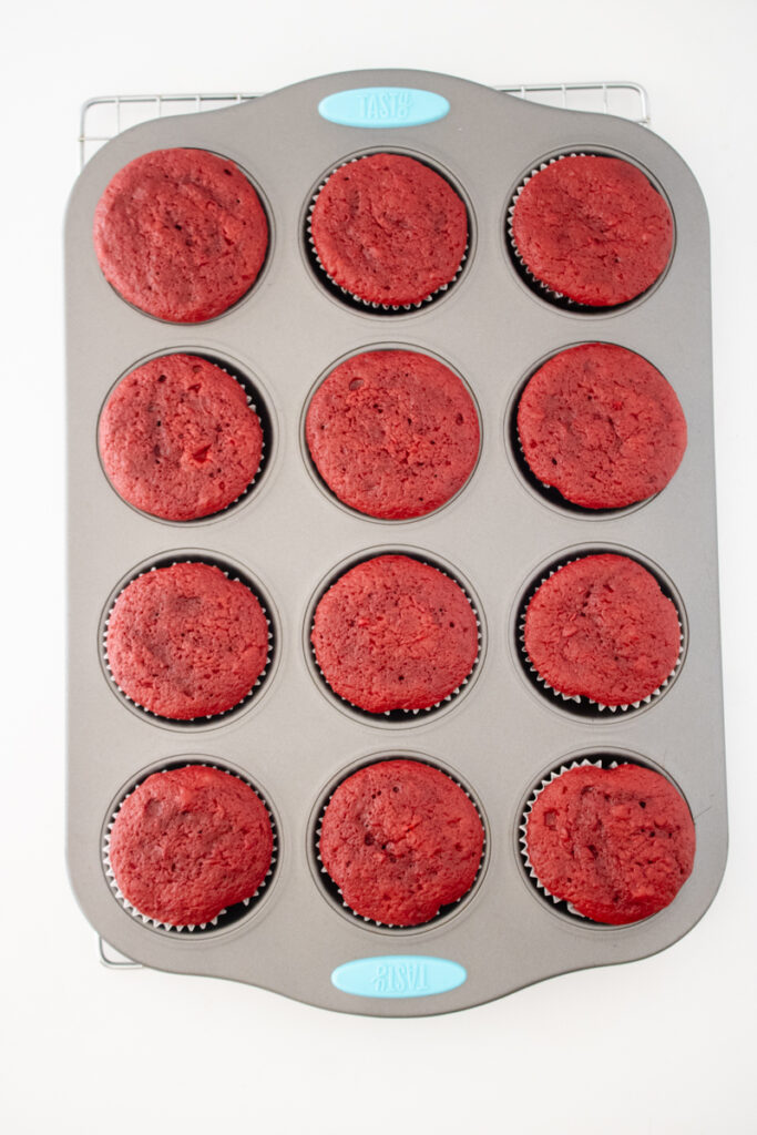 Freshly baked red velvet cupcakes cooling in a muffin pan.