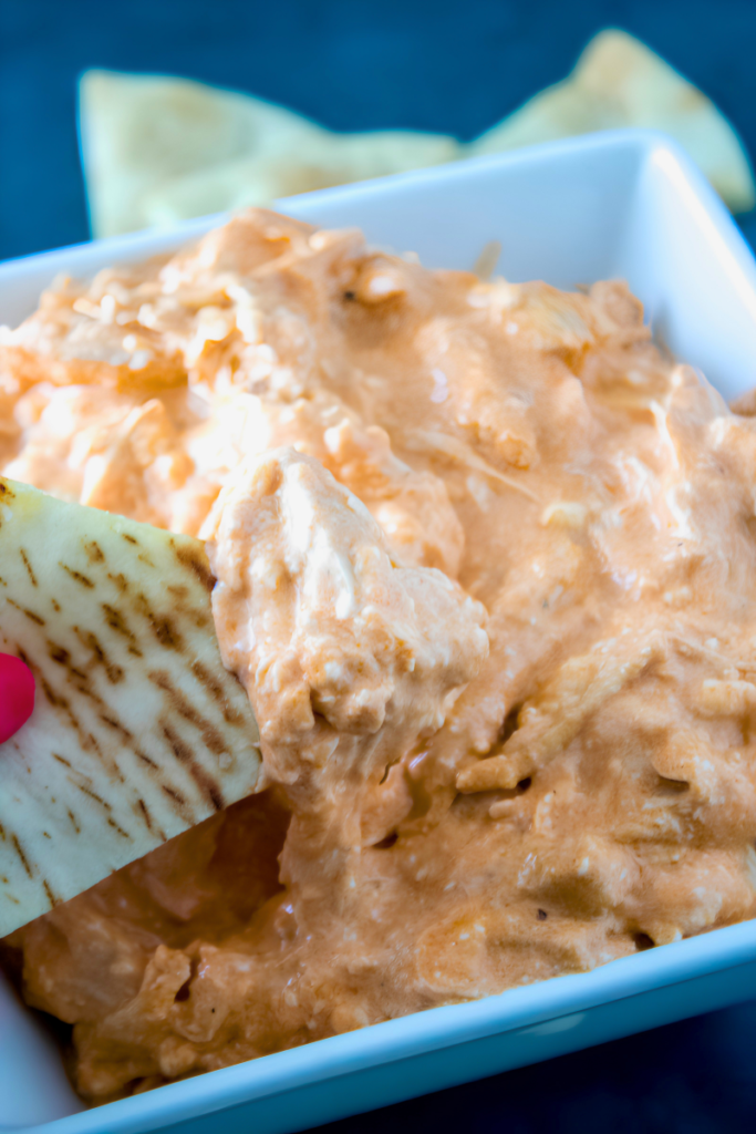 Pita chip dipped into creamy buffalo chicken dip with shredded rotisserie chicken.