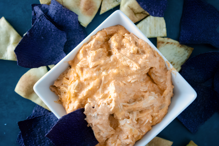 Creamy buffalo chicken dip made with rotisserie chicken served in a white bowl with blue and white tortilla chips.