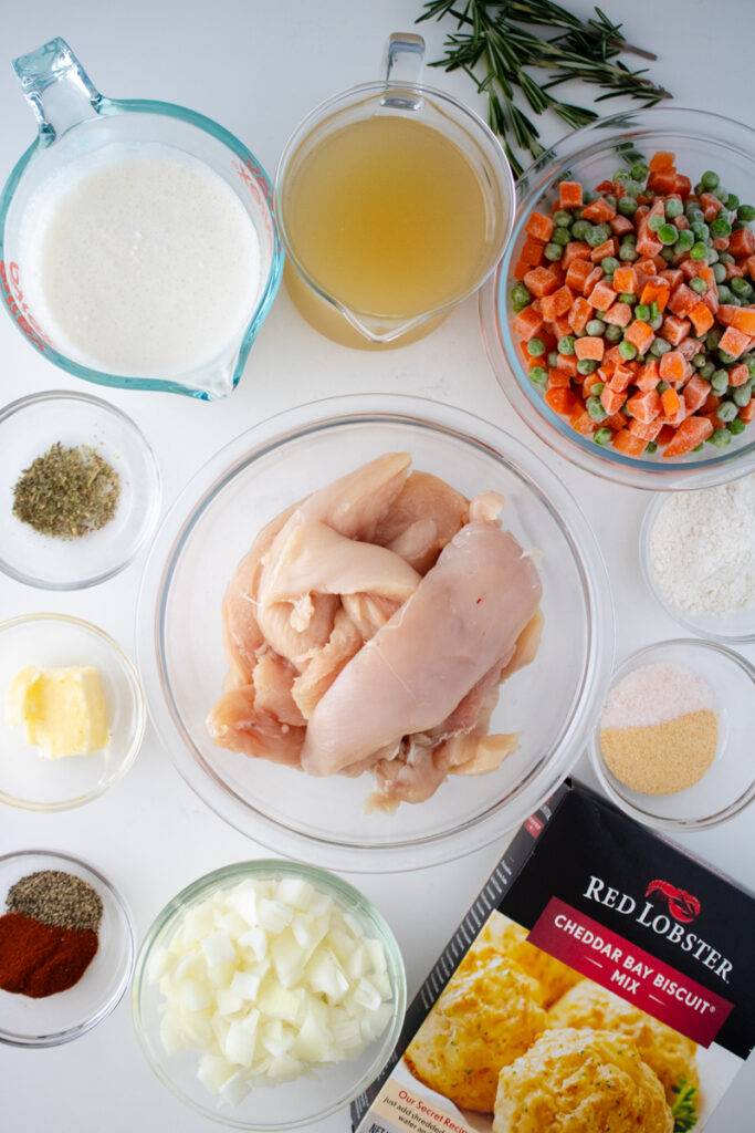 Ingredients for chicken and dumplings with biscuit mix, including chicken breasts, frozen peas and carrots, chicken broth, heavy cream, diced onion, seasonings, and Red Lobster Cheddar Bay Biscuit Mix.