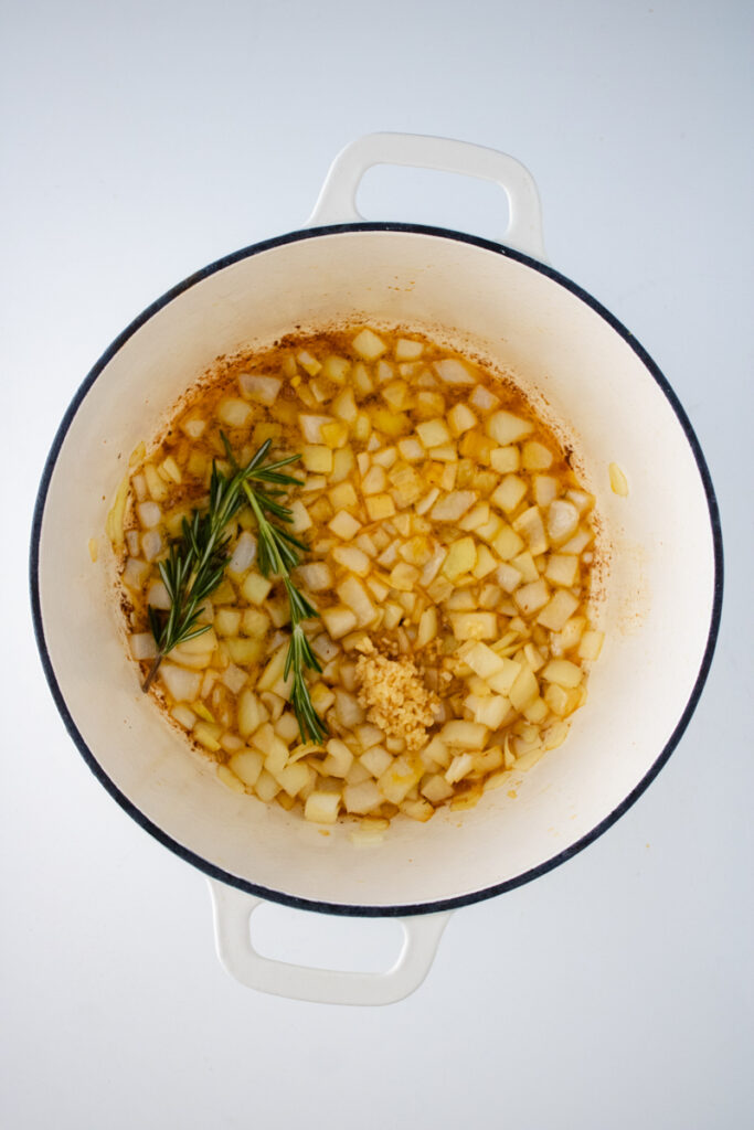 Diced onion, minced garlic, and fresh rosemary cooking in a Dutch oven for chicken and dumplings with biscuit mix.