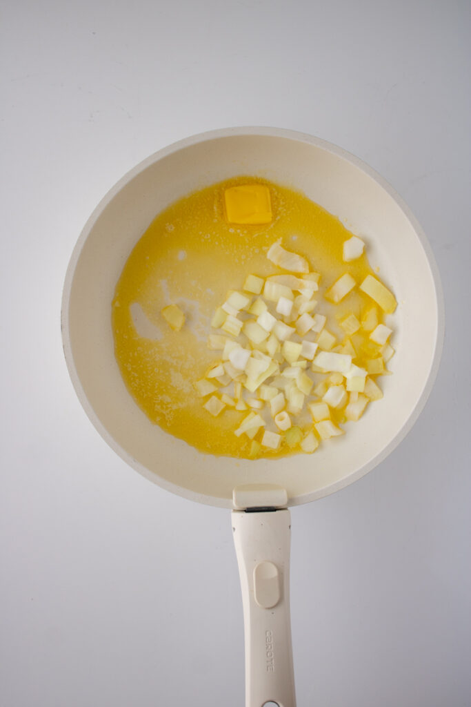 Diced onions cooking in melted butter in a skillet for chicken pot pie with biscuits.