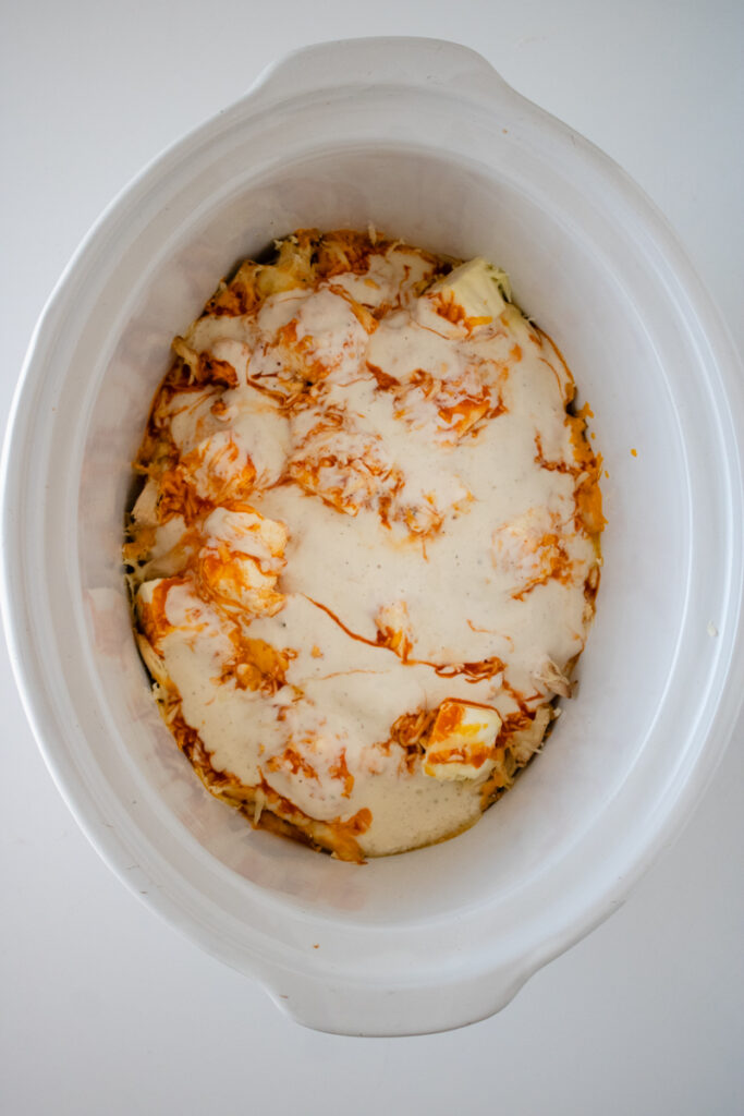 Buffalo chicken dip ingredients melting together in a slow cooker before being stirred.
