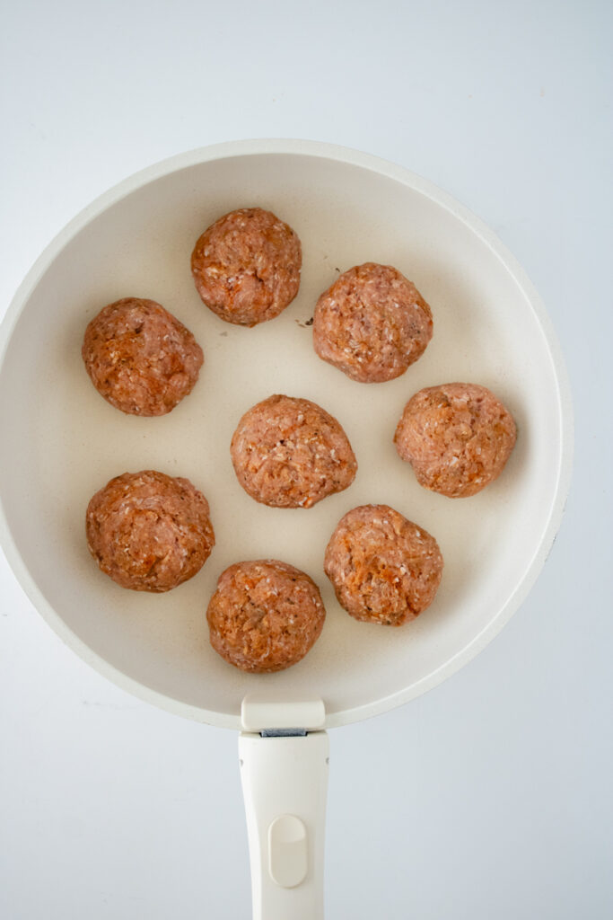 Raw homemade turkey sausage patties cooking in a skillet before being flipped.