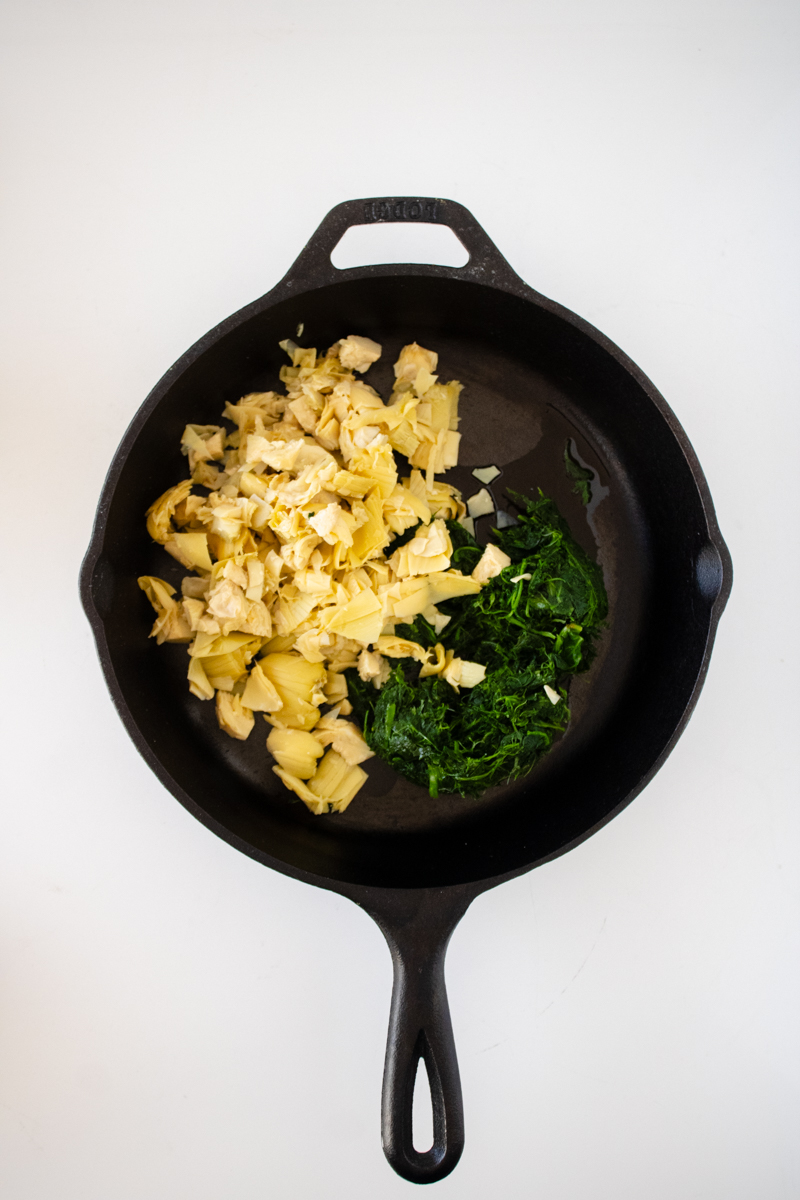 Thawed frozen spinach and chopped artichoke hearts in a cast iron skillet before cooking.