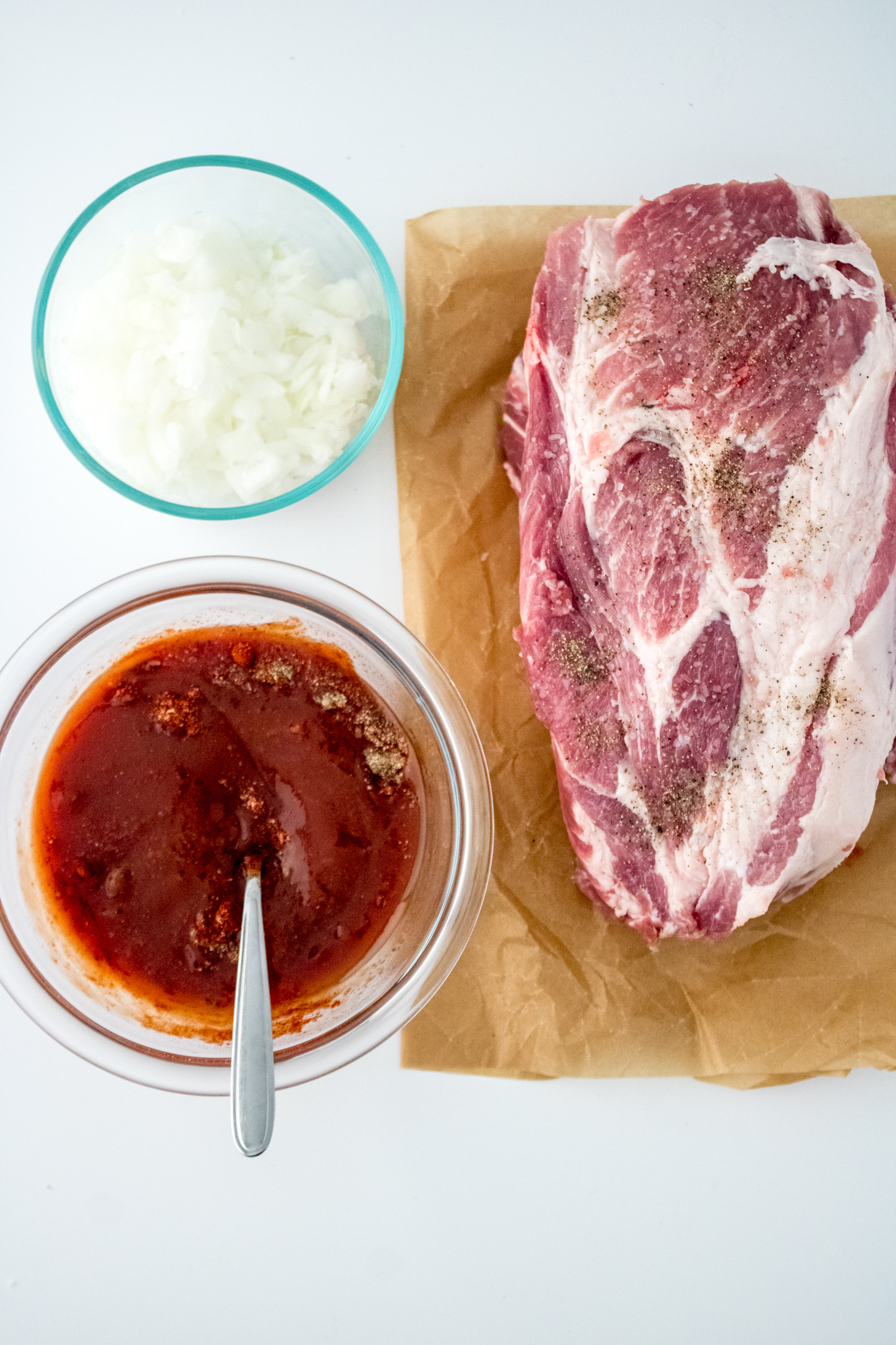 Homemade barbecue sauce being mixed for Crock Pot BBQ Pulled Pork beside a seasoned pork shoulder.