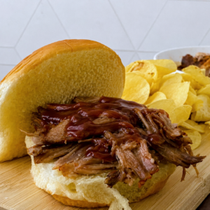 Crock Pot BBQ Pulled Pork sandwich topped with barbecue sauce and served with potato chips.
