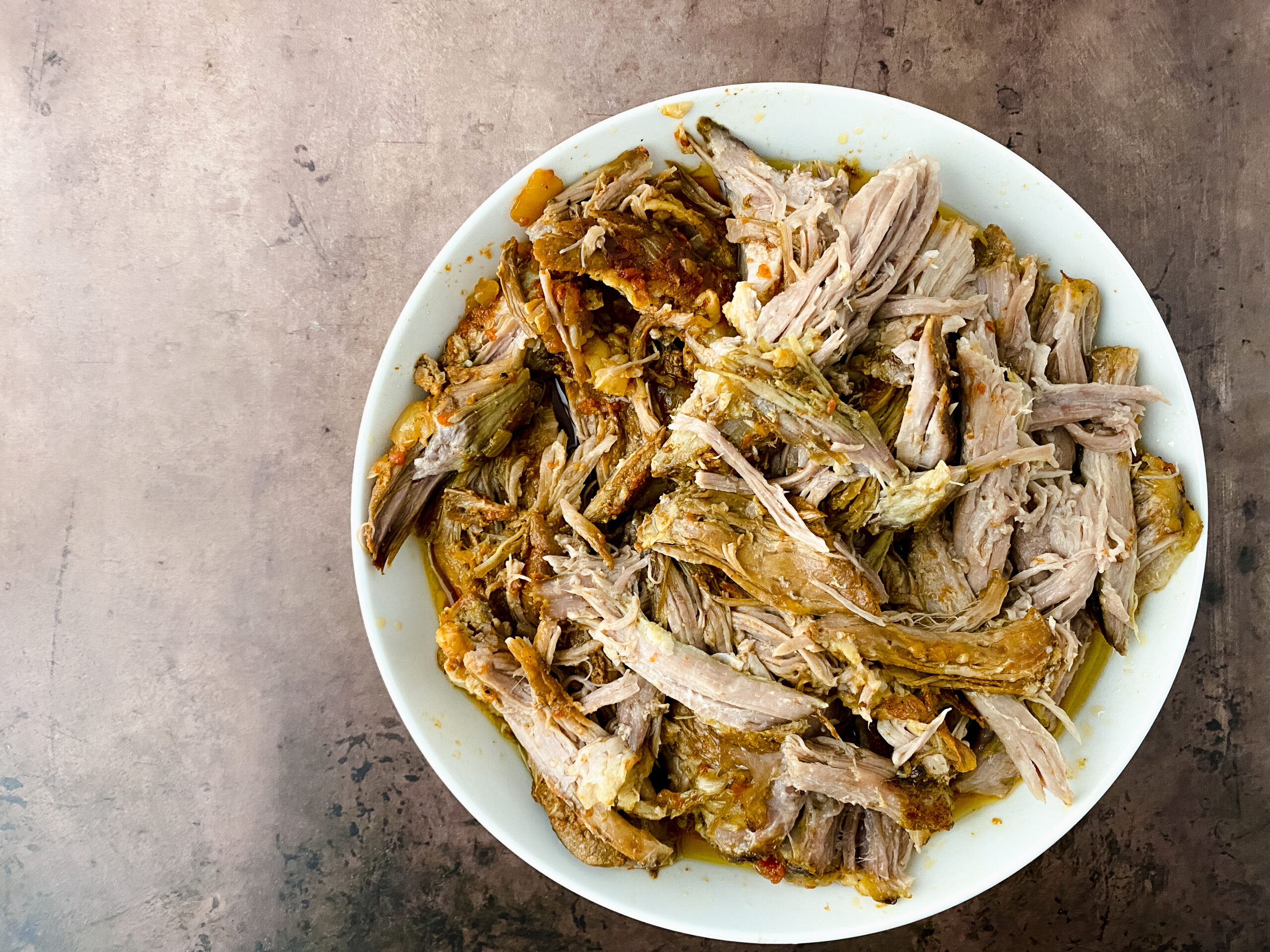 Shredded Crock Pot BBQ Pulled Pork in a white bowl before being mixed with the cooking juices.