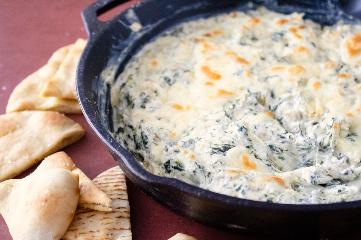 Creamy spinach artichoke dip baked in a cast iron skillet and served with warm pita bread for dipping.