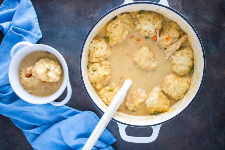 Overhead view of creamy chicken and dumplings made with Cheddar Bay biscuit mix, shredded chicken, and frozen vegetables in a white Dutch oven.