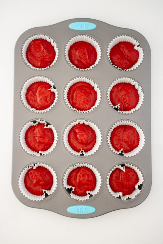 Red velvet cupcake batter portioned into cupcake liners before baking.