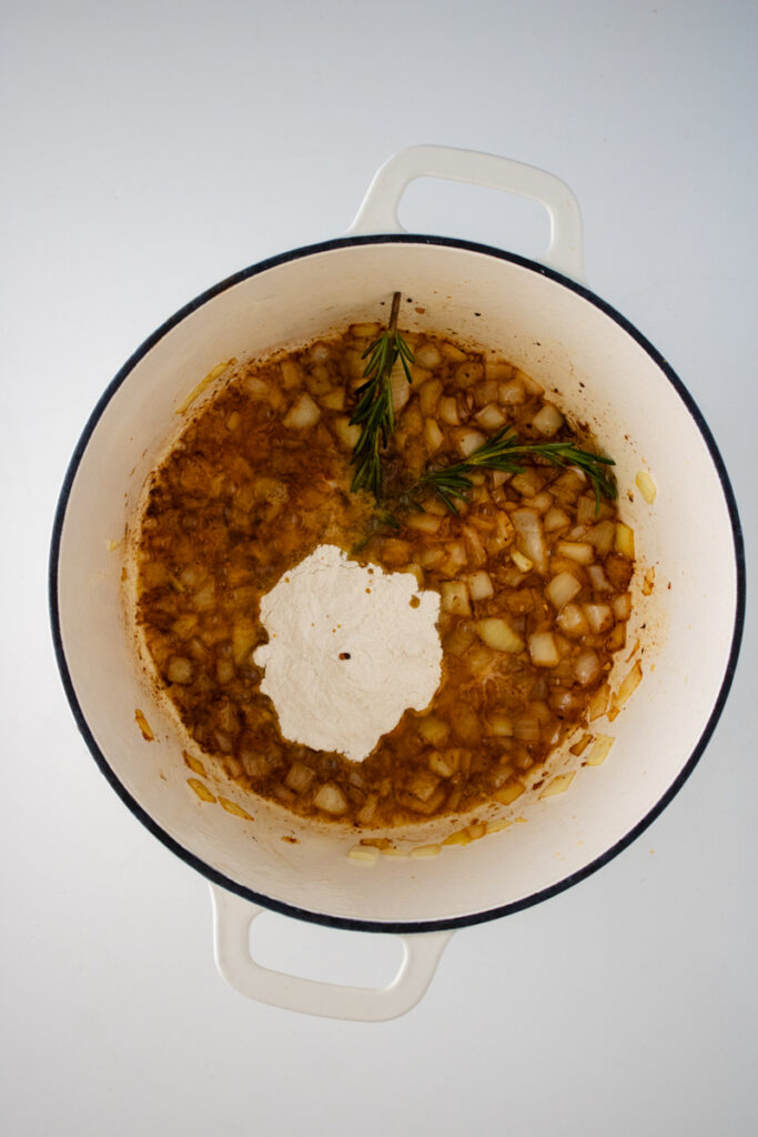 Flour added to butter, onion, garlic, and rosemary in a Dutch oven to make a roux for chicken and dumplings with biscuit mix.