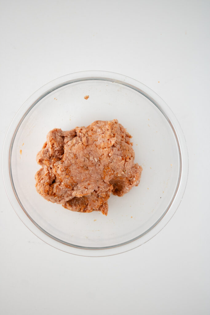 Seasoned ground turkey mixed together in a glass bowl for homemade turkey sausage.