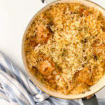 Overhead view of one pot chicken and rice made with seasoned chicken thighs, fluffy basmati rice, onions, and simple pantry spices cooked together in a large skillet.