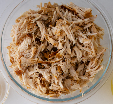 Shredded rotisserie chicken in a glass bowl prepared for chicken pot pie with biscuits.