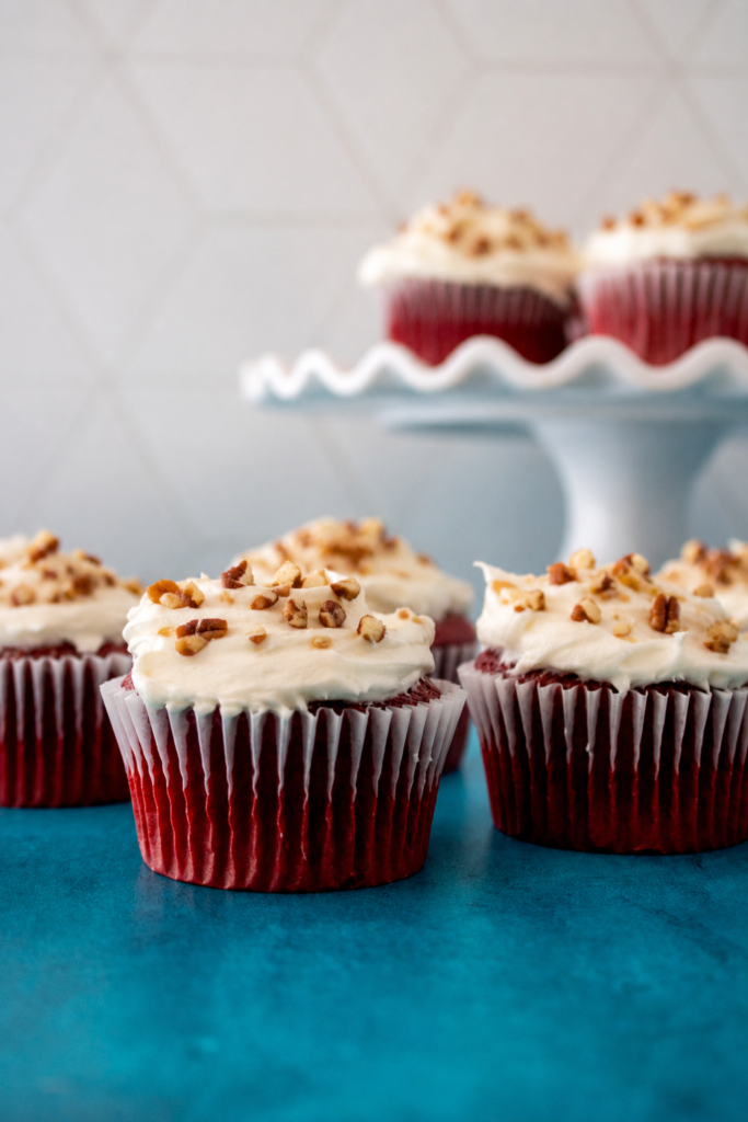 Red velvet cupcakes topped with cream cheese frosting and a light pecan garnish.