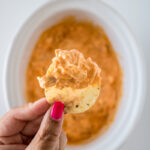 Tortilla chip topped with creamy buffalo chicken dip held in front of a slow cooker.