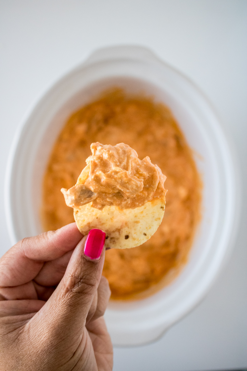 Tortilla chip topped with creamy buffalo chicken dip held in front of a slow cooker.