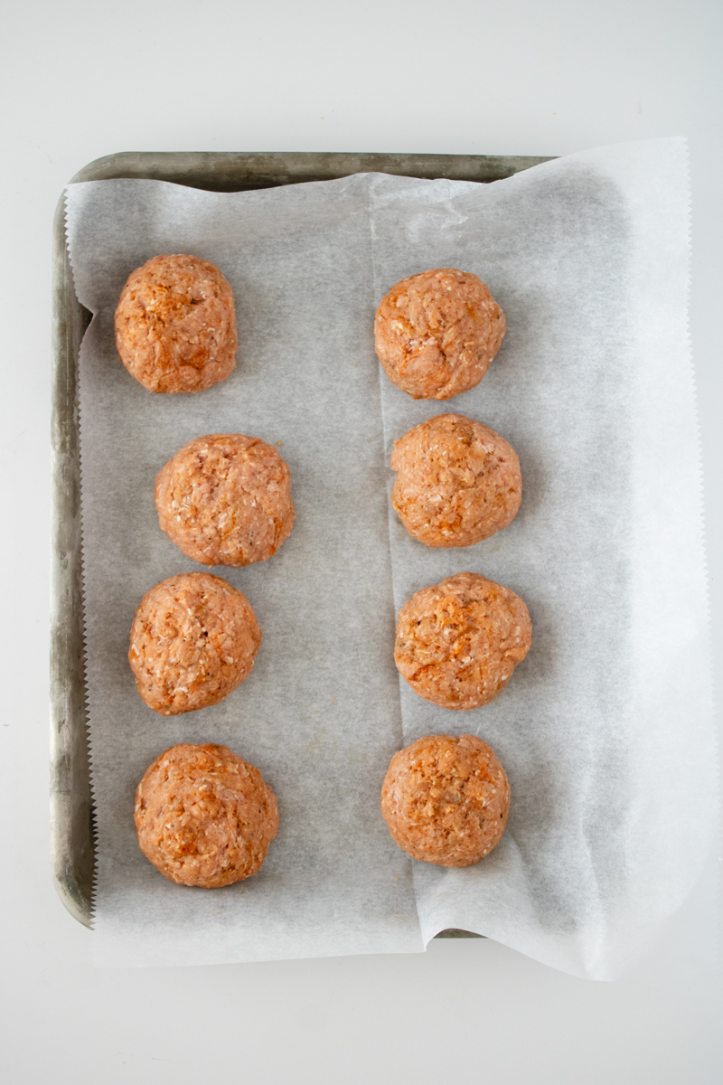 Portions of homemade turkey sausage mixture shaped into patties on a parchment-lined baking sheet.