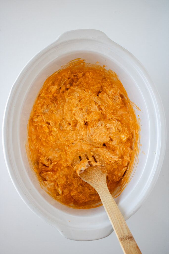 Creamy buffalo chicken dip being stirred in a slow cooker after the cheeses have melted.