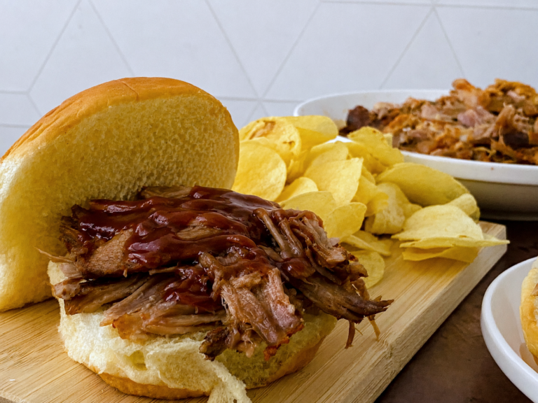 Crock Pot BBQ pulled pork sandwich topped with barbecue sauce and served with potato chips.